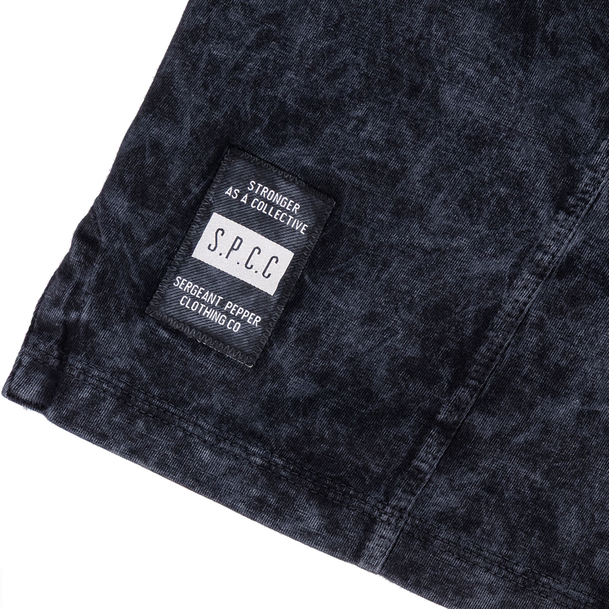 Close-up of the SPCC woven badge on the Rodgers Tee - Black, showcasing the unique garment-washed texture.