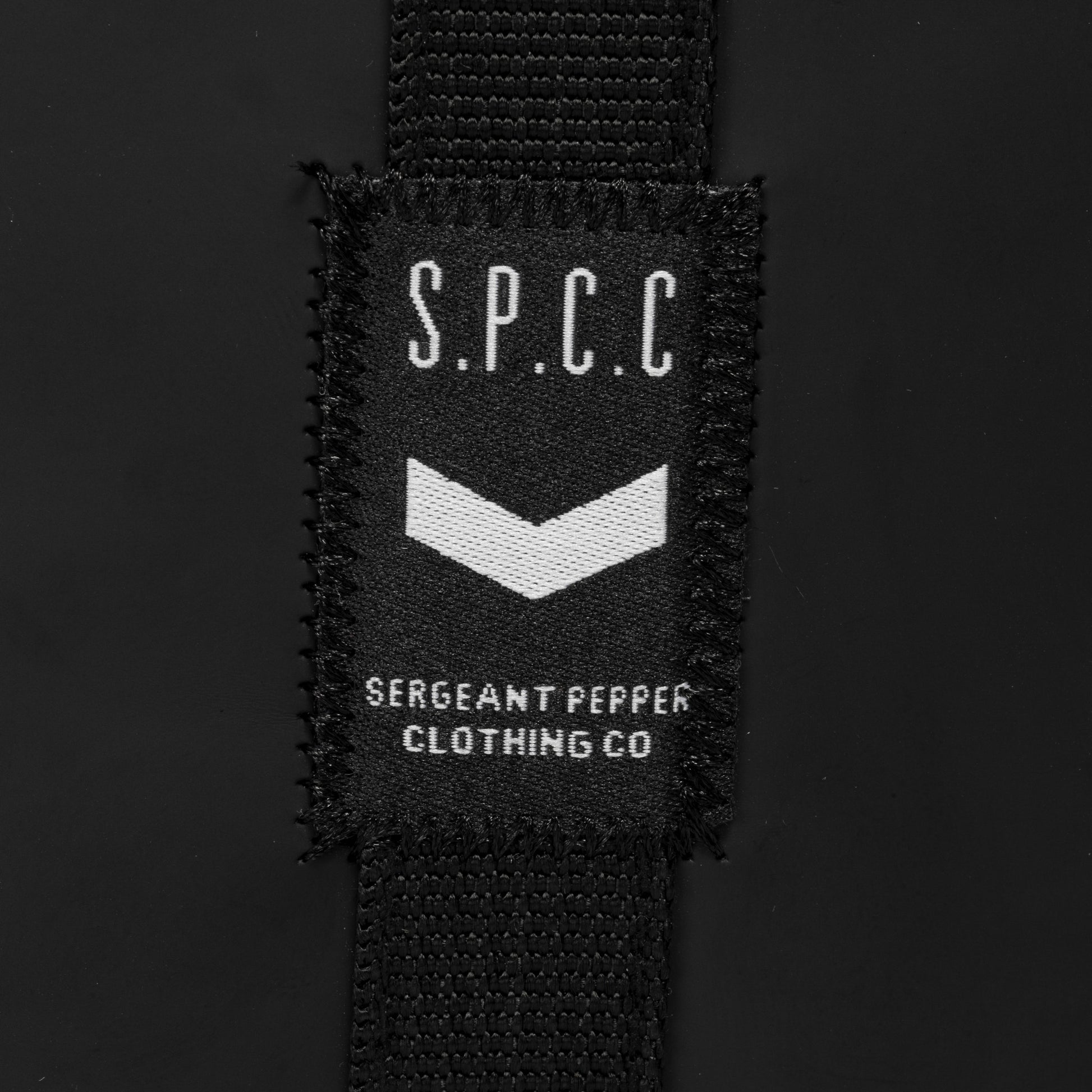 Label showcasing S.P.C.C. logo on the Surge Atlas Hip Bag - Black, highlighting its stylish branding.